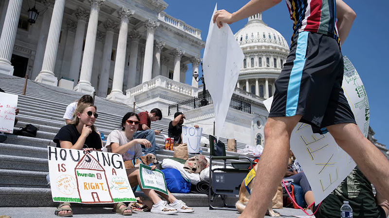  Protesters advocating for housing rights on the steps of a government building, holding signs with messages like "Housing is a Human Right.