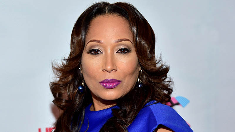 Chrystale Wilson in a royal blue outfit, smiling confidently with long wavy hair and vibrant purple lipstick.