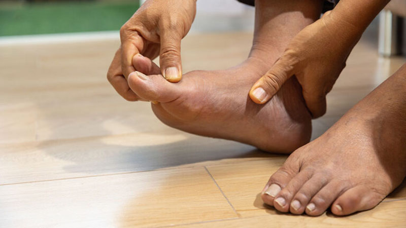 A close-up of hands massaging a foot, symbolizing relief from gout pain, with a wooden floor background.