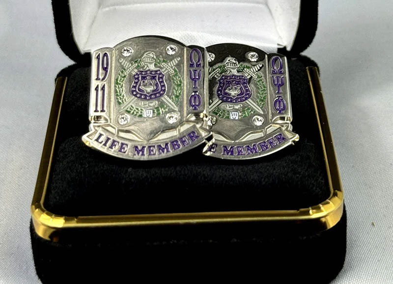 Pair of silver Omega Psi Phi Life Member cufflinks resting on a purple dress shirt cuff.