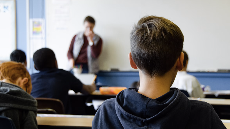 Elementary students seated at desks in a classroom facing their teacher, highlighting twin cities public health gaps in school vaccination coverage