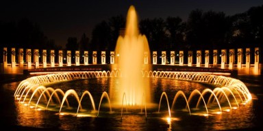 Illuminated Washington D.C. monuments reflecting over the water under the night sky.