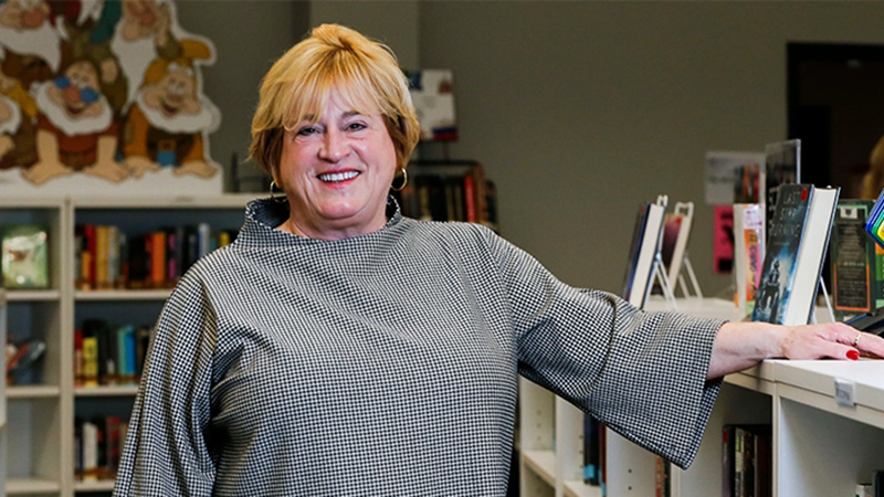 Missouri policy roundup report on DESE leader Karla Eslinger smiling inside a school library surrounded by bookshelves.