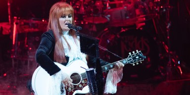 Country music icon Wynonna Judd singing live under warm stage lights with a microphone