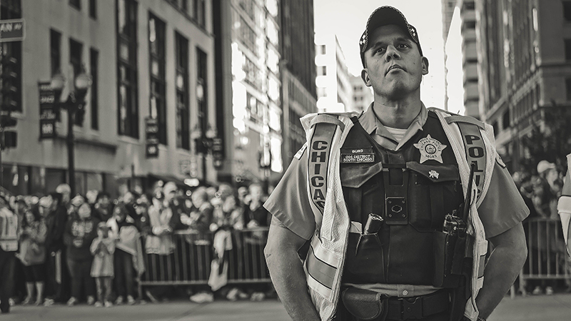 Black and white photograph of a uniformed Chicago police officer standing duty in a high-visibility vest during a downtown public event