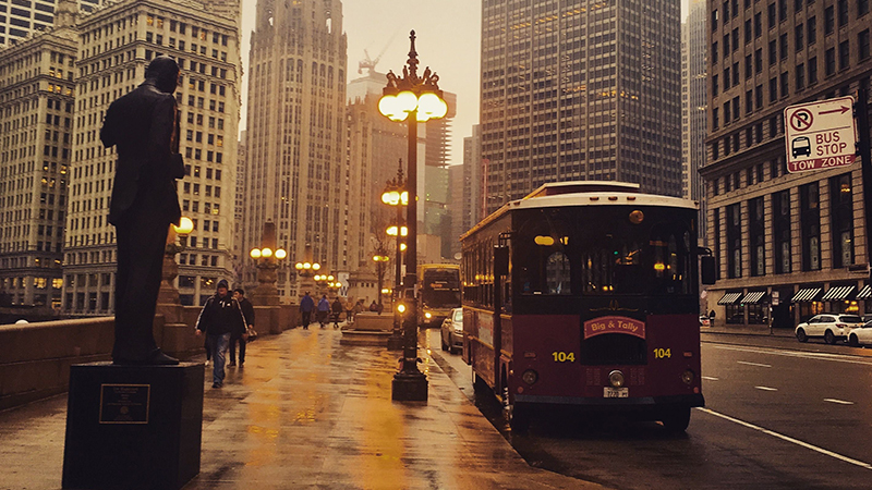 Chicago trolley bus driving along the DuSable Bridge near the Wrigley Building and Tribune Tower on a wet evening.