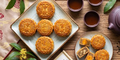 Overhead view of traditional patterned Chinese mooncakes served with hot tea in ceramic cups on a blue table.