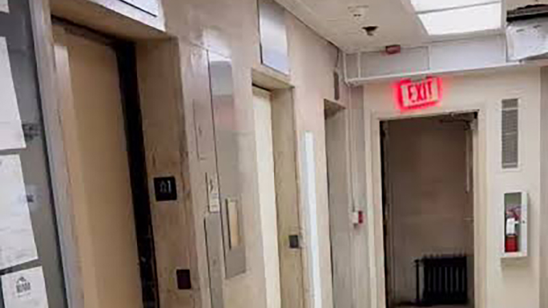 Out-of-service passenger elevator doors and emergency exit corridor in an aging residential apartment hallway.