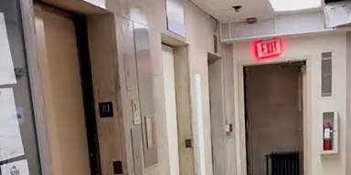 Out-of-service passenger elevator doors and emergency exit corridor in an aging residential apartment hallway.