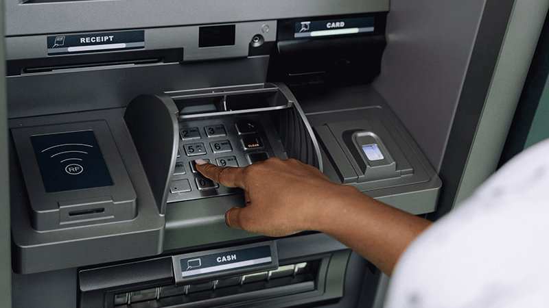A person enters their PIN on a metallic ATM keypad while managing a bank deposit and cash withdrawal.