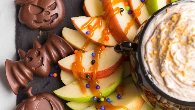 A festive Halloween party table filled with banana ghosts, clementine pumpkins, and apple monster mouths.