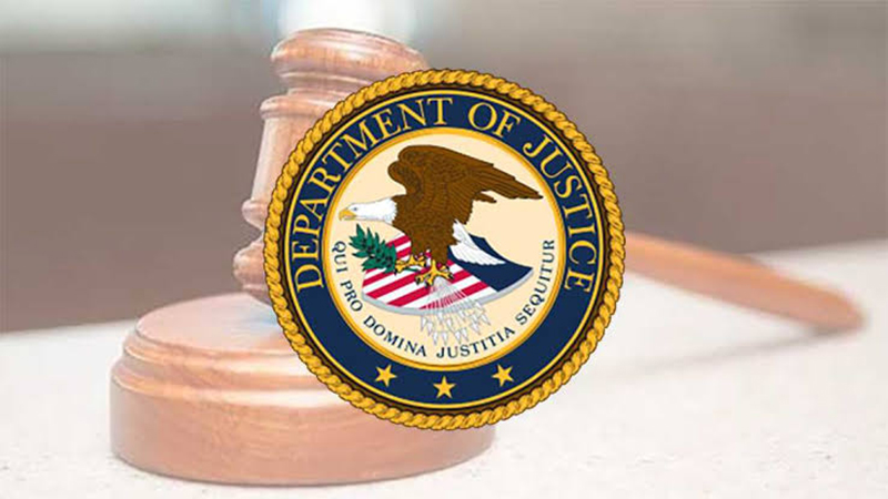 United States Department of Justice seal overlaid on a wooden judge's gavel and sound block in a federal courtroom.