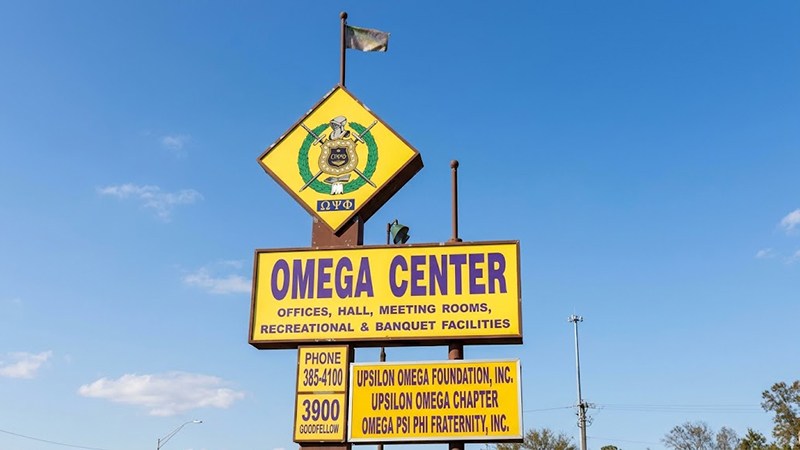 The official yellow and purple outdoor roadside sign for the Omega Center at 3900 Goodfellow Boulevard featuring the Omega Psi Phi Fraternity emblem.