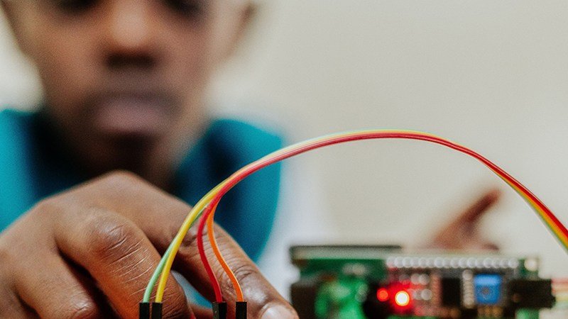 A focused student working on an electronics circuit board with colorful jumper wires.