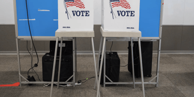 Two white voting privacy booths with the American flag and the word VOTE printed on the front, set up inside a polling location.