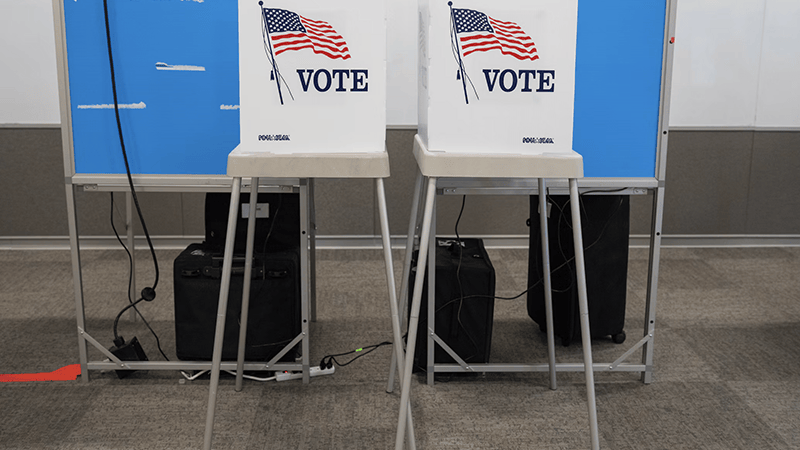 Two white voting privacy booths with the American flag and the word VOTE printed on the front, set up inside a polling location.