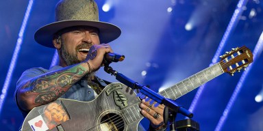 Zac Brown Band performing live with military brass instrumentalists on a large concert stage.